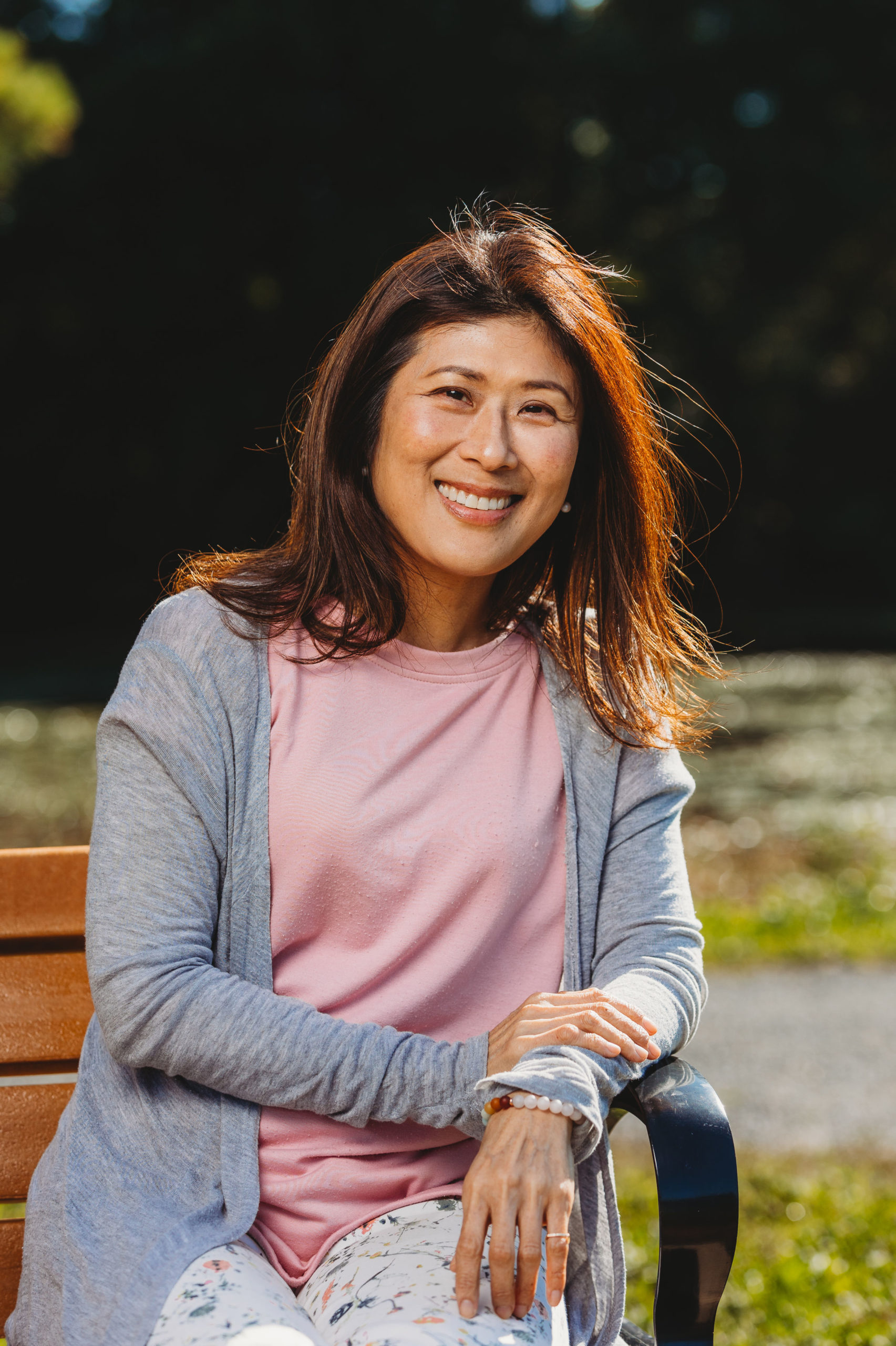 Therapist Fusako, smiling warmly, sitting relaxed by the water in Ashley Reservoir, Holyoke, MA.