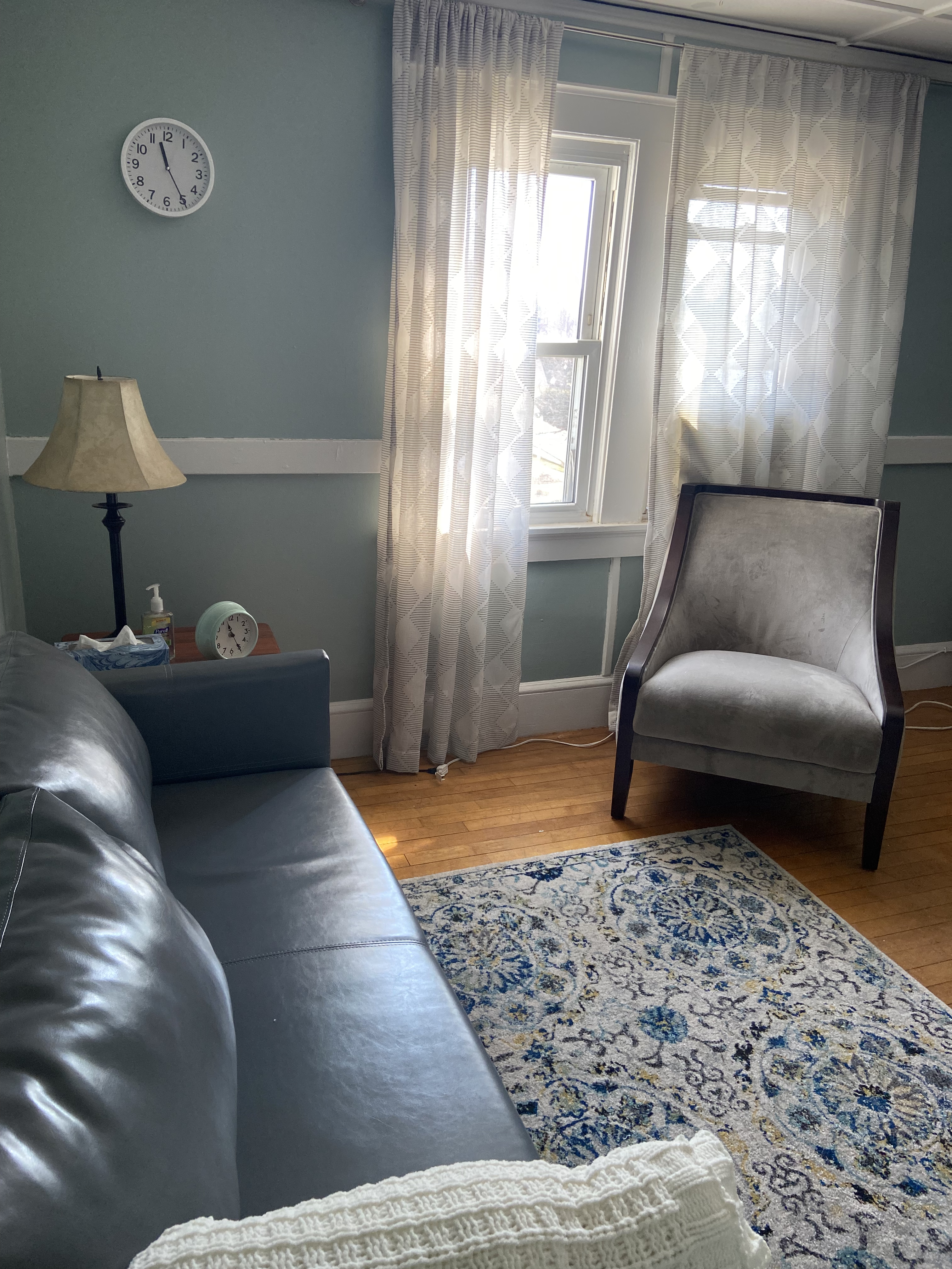 A therapist's office has a light blue wall and gray sofas on the wood floor. Cream color blanket is on the sofa.