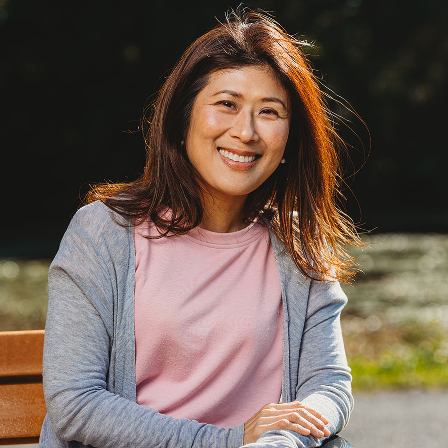 Fusako Yamagiwa sits on a bench, smiling, in casual clothes on a sunny day.